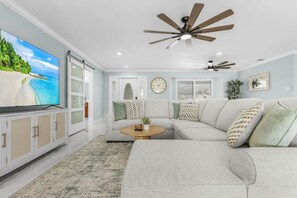 A living room with a sectional sofa, a television, a ceiling fan, and a clock on the wall. - Panoramic Water Views • Gulf Access • No Bridges (Cape Coral)