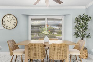 A dining room with a wooden table, four wicker chairs, a white vase with flowers, and a large wall clock. - Panoramic Water Views • Gulf Access • No Bridges (Cape Coral)