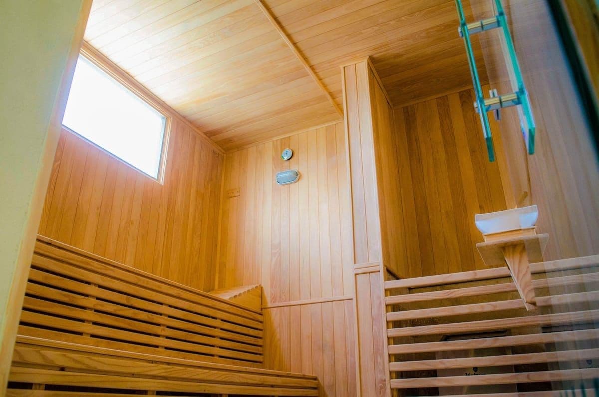 A wooden sauna with a sloped ceiling, a window, and a wooden bench.