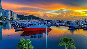Un puerto deportivo con barcos amarrados, un barco rojo al frente y edificios al fondo.