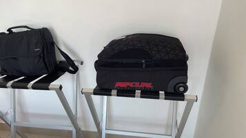 A black bag and a black wheeled bag on a metal table against a white wall.