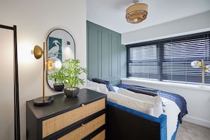 Un dormitorio con cama, mesita de noche, lámpara, espejo y ventana con persianas.