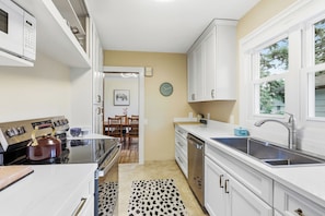 A compact kitchen with white cabinetry, a built-in oven, a microwave, and a sink. - Urban Oasis w/ 10 beds•Sauna•Solar•Wellness Studio•Fenced Yard•Garage (Falcon Heights)
