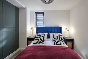 Ein Schlafzimmer mit einem Bett, einem Fenster mit Jalousien, Nachttischlampen und einem dunkelbraunen Kleiderschrank.