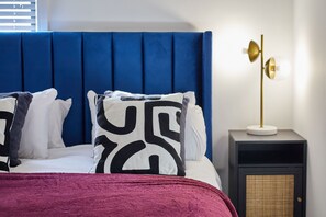 Una cama con cabecera azul, almohadas estampadas en blanco y negro, y una manta roja.