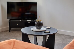 Ein modernes Wohnzimmer mit einem runden Tisch, einem dekorativen Gegenstand auf dem Tisch und einem Fernseher auf einem Schrank.