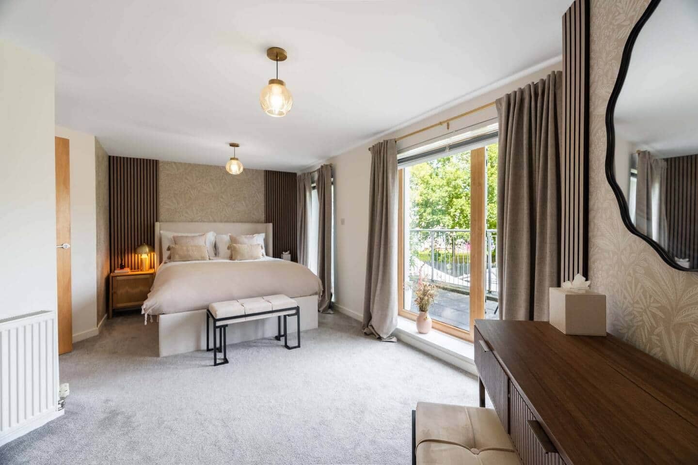 Een ruime slaapkamer met een groot bed, nachtkastjes, een dressoir, een bankje en uitzicht op de omgeving.