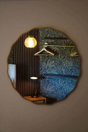 A circular mirror with a wooden frame, a hanging light fixture, and a wall with a floral pattern. - Lochburn House | Garden, Parking & Stylish 3BR (Glasgow)