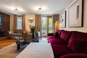 A living room with a sofa, armchair, coffee table, and a red couch. There is a mirror on the wall and a window with curtains. - Lochburn House | Garden, Parking & Stylish 3BR (Glasgow)