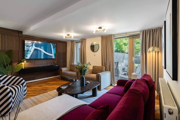 A modern living room with a flat-screen TV, comfortable seating, and a view of the outdoors. - Lochburn House | Garden, Parking & Stylish 3BR (Glasgow)