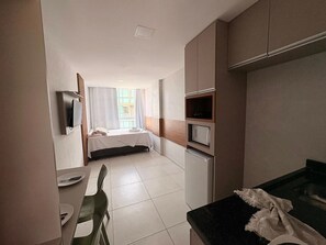 A hotel room with a bed, a small kitchenette, a dining table, and a TV. - Eco Mirage Residence por YOLO (Ipojuca)