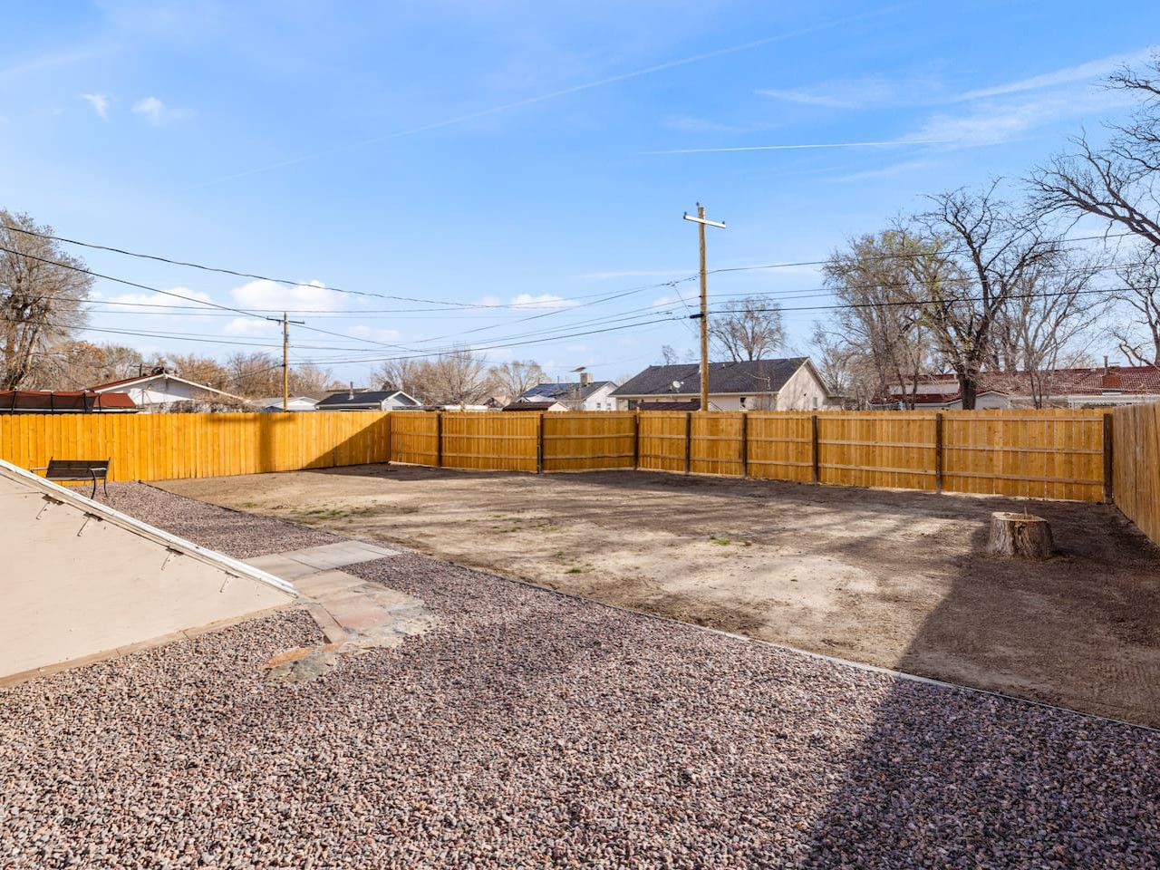 A backyard with a wooden fence, gravel ground, and a concrete patio.