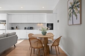 A modern kitchen with white cabinets, a dining table with chairs, and a coffee machine. - Balcony 2-bed Apartment Near Albert Park (Melbourne)