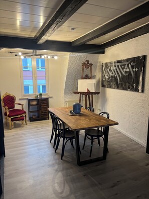 A dining area with a wooden table, black chairs, a red upholstered chair, and a window with blinds. - Vrbo Property (Euskirchen)
