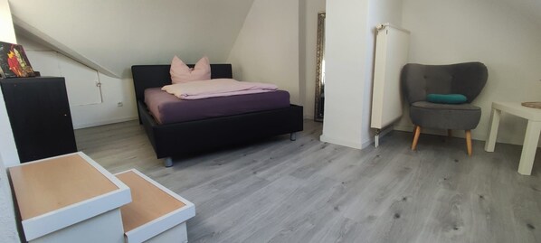 A bedroom with a bed, a chair, a small table, and a radiator. - Attic Duplex Apartment (Euskirchen)