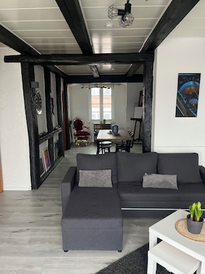 A modern living room with a sectional sofa, a dining area with a table and chairs, and a kitchen in the background. - Vrbo Property (Euskirchen)