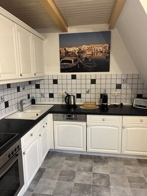 A kitchen with white cabinets, a black countertop, and a tiled backsplash. - Attic Duplex Apartment (Euskirchen)