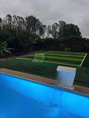 Een zwembad met een fontein en een voetbalveld met doelen.