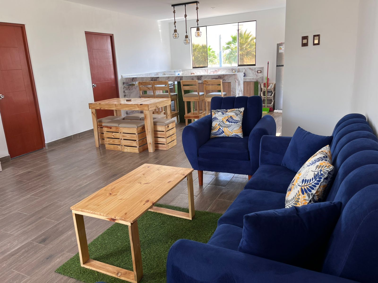 A modern living room with a blue sofa, wooden coffee table, and a dining area with a wooden table and chairs.
