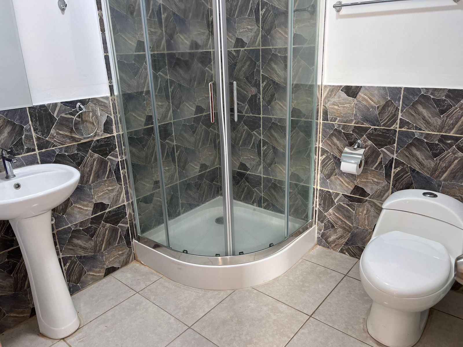 Un bagno con cabina doccia in vetro, lavabo su piedistallo e water.