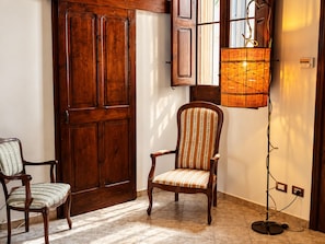 A room with a wooden door, two upholstered chairs, a floor lamp, and a tiled floor. - LIVING IN Ástricu (Lecce)