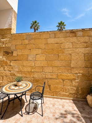 A patio with a round table and chairs, a potted plant, and a stone wall. - LIVING IN Ástricu (Lecce)