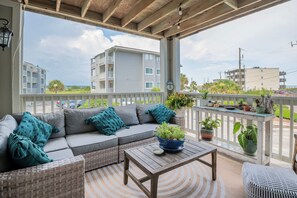 A covered outdoor seating area with a gray sofa, teal cushions, and a wooden table. - The Breakers Paradise - New Listing (Carolina Beach)