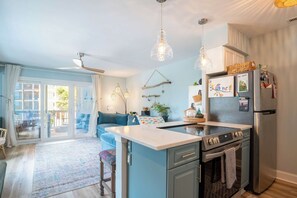 A modern kitchen with a central island, stainless steel appliances, and a dining area with a blue sofa. - The Breakers Paradise - New Listing (Carolina Beach)