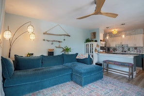 A modern living room with a sectional sofa, a dining area with a kitchen in the background, and a ceiling fan. - The Breakers Paradise - New Listing (Carolina Beach)