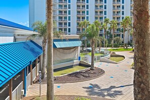 A hotel courtyard with palm trees, a pool, and a building with a blue roof. - ⛱️Palms 2203 - Beach Nearby + Lagoon Pool + Free Seasonal Shuttle⛱️ (Destin)