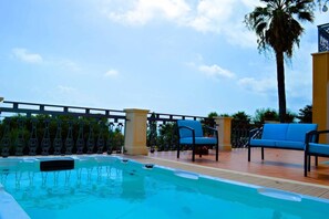 Ein Pool mit Fliesen und eine Liegefläche mit zwei blauen Liegestühlen und einer Palme.