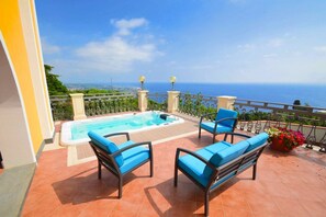 Eine Dachterrasse mit Whirlpool, zwei blauen Sitzgelegenheiten und Blick auf das Meer.