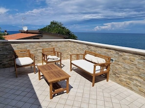 A patio with stone walls, a wooden table, and two wooden chairs with cushions. - Villa Daniela con Piscina Privata e Discesa a Mare (Augusta)