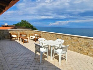 An outdoor patio with a stone wall, a wooden table, and white plastic chairs. - Villa Daniela con Piscina Privata e Discesa a Mare (Augusta)