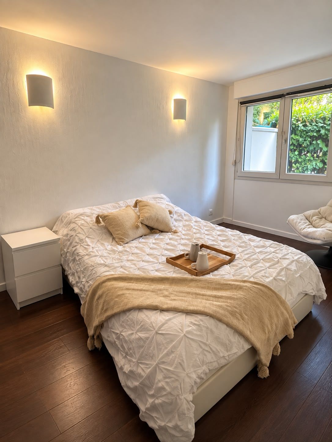 Une chambre à coucher avec un lit, des tables de chevet, une fenêtre donnant sur un beau paysage et un fauteuil.
