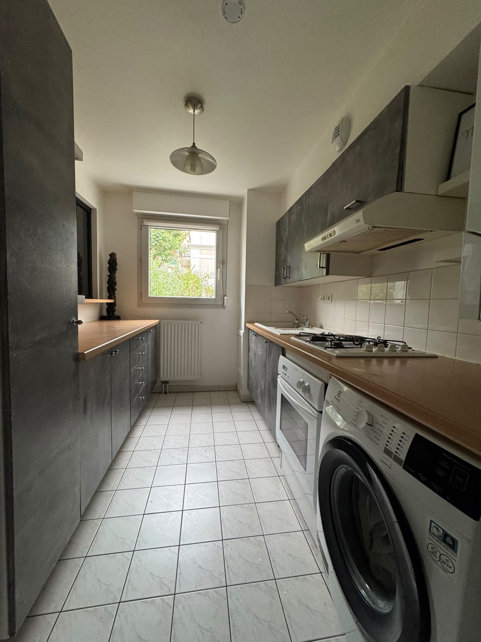 Une cuisine compacte équipée d’un lave-linge intégré, d’une fenêtre et d’un radiateur.