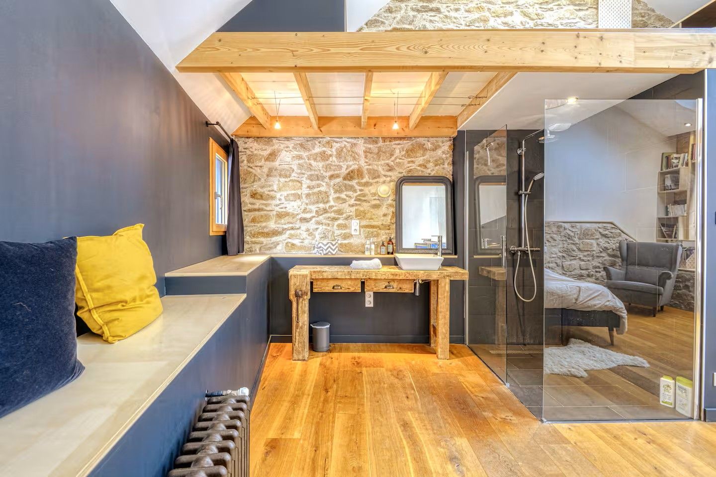Un baño moderno con pared de piedra, banco de madera y cabina de ducha de vidrio.