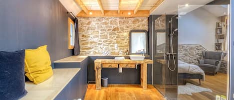 A modern bathroom with a stone wall, wooden bench, and a glass shower enclosure.