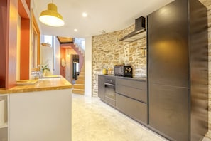 A modern kitchen with a stone wall, stainless steel appliances, and a wooden countertop. - Hostcare - Maison unique dans ancien bar rénové (Nantes)