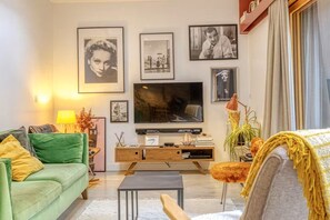A living room with a green sofa, a coffee table, a flat-screen TV, and a bookshelf. - Hostcare - Maison unique dans ancien bar rénové (Nantes)