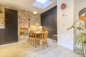 A modern kitchen with a stone wall, a skylight, and a dining area with wooden furniture. - Hostcare - Maison unique dans ancien bar rénové (Nantes)