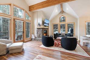 A spacious living room with a fireplace, large windows, and a television. - Snowflake Lift 3-Min Walk | Main St | Private Hot Tub (Breckenridge)