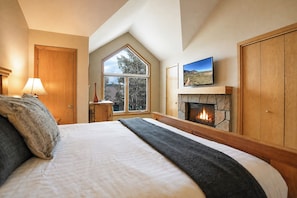 A bedroom with a large bed, a fireplace, a window with a view, and a television on the wall. - Snowflake Lift 3-Min Walk | Main St | Private Hot Tub (Breckenridge)