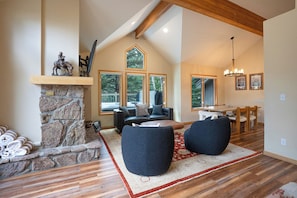 A spacious living area with a stone fireplace, a large window, and a dining area. - Snowflake Lift 3-Min Walk | Main St | Private Hot Tub (Breckenridge)