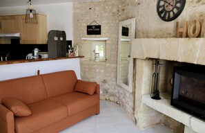 Un salon comprenant un canapé, une cheminée, un coin cuisine et un mur en pierre.