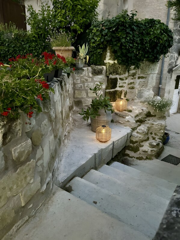 A stone staircase with steps leading up to a landing, surrounded by greenery and potted plants.