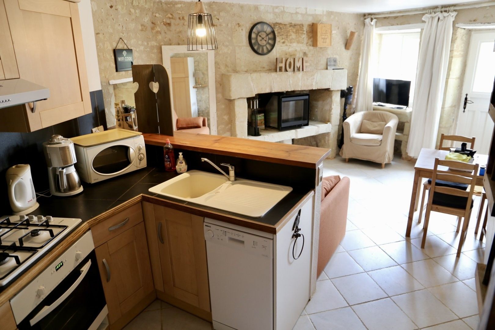 Cocina compacta equipada con lavavajillas, microondas y estufa. Cuenta con un comedor con mesa y sillas, además de una chimenea con un reloj encima.