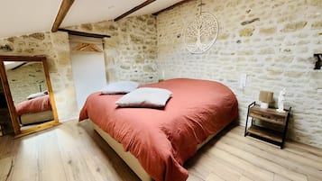 Une chambre avec un mur en pierre, un lit recouvert d’une courtepointe rouge, un plancher en bois et une lucarne.
