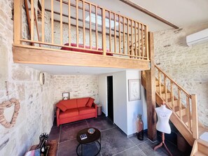 Un espai tipus loft amb una escala de fusta, un sofà vermell, una taula petita i un maniquí.