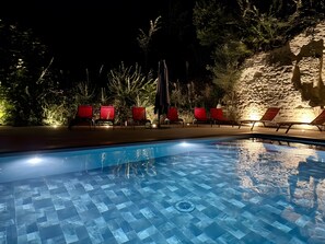 Une piscine dont le fond est carrelé, entourée de chaises longues rouges et d’un mur en pierre.
